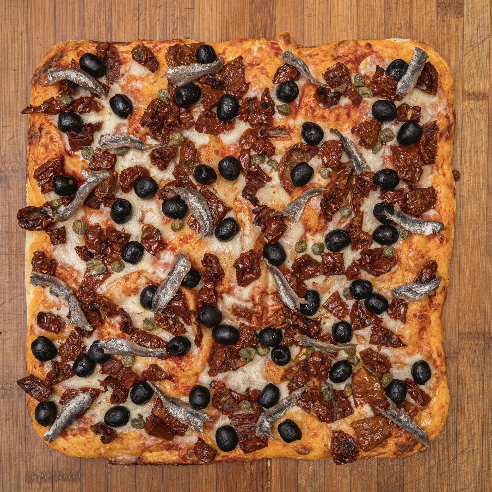 TRANCIO DI PIZZA CON POMODORO, MOZZARELLA, POMODORI SECCHI, ACCIUGHE, CAPPERI E OLIVE