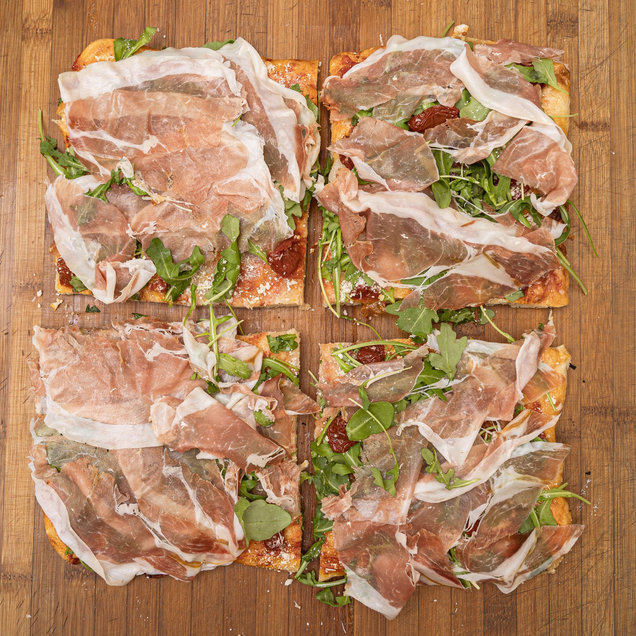 TRANCIO DI PIZZA CON POMODORO, RUCOLA, BUFALA DOP, OLIVE DI TAGGIA, GRANA E CRUDO DI PARMA