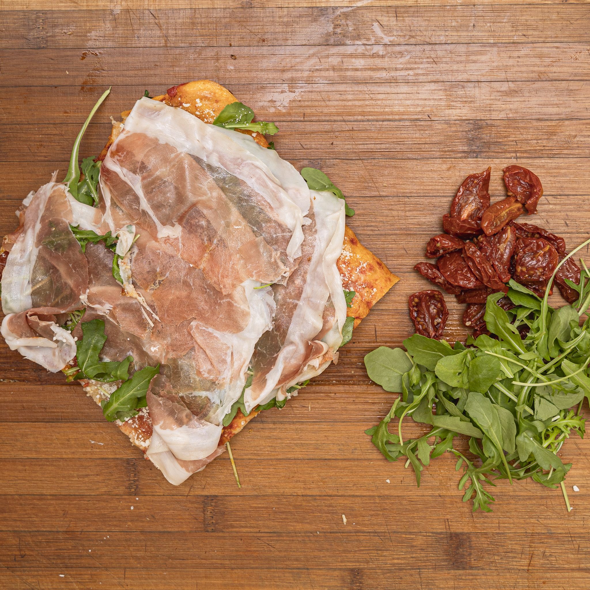 TRANCIO DI PIZZA CON POMODORO, RUCOLA, BUFALA DOP, OLIVE DI TAGGIA, GRANA E CRUDO DI PARMA
